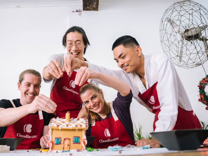 Four people decorating a gingerbread house